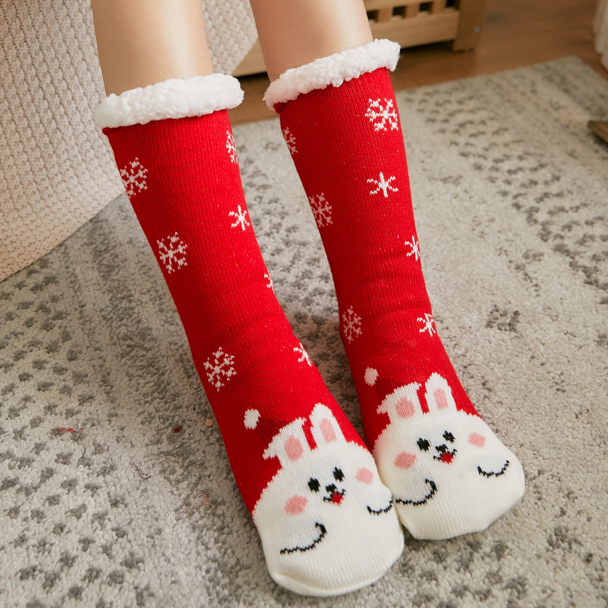 Red socks with white snowflakes and bunny faces on a carpeted floor.